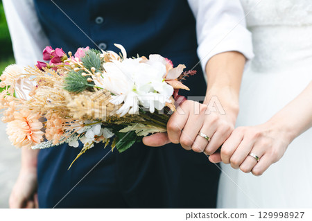 新娘和新郎的手拿著結婚戒指和花束 新娘和新郎的手拿著結婚戒指和花束 129998927