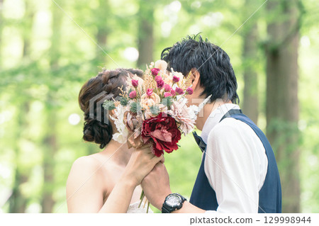 Bride and groom kissing over bouquet 129998944