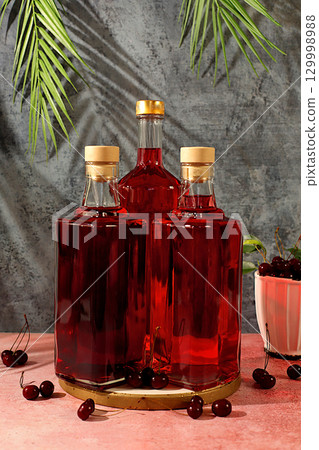 Homemade strong cherry cider in bottles and glasses on elegant background, still life with alcoholic drinks and fresh cherries, home winemaking concept, minimalist banner for bar 129998988