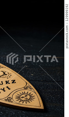 A close-up view of a light brown wooden Ouija planchette with carved sun and moon symbols resting on a dark, textured surface, offering ample copy space. 129999192