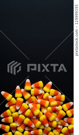 A vibrant pile of classic candy corn with yellow, orange, and white segments is neatly arranged at the bottom of a dark textured background, offering ample copy space. 129999193