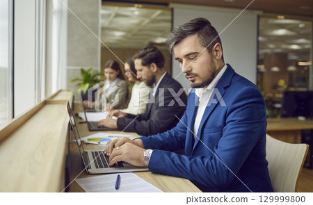 Young man and other business people working on laptops in modern coworking space Young man and other business people working on laptops in modern coworking space 129999800