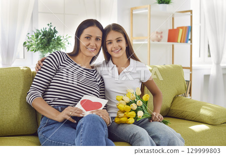 Loving daughter gives card and bouquet of beautiful flowers to mother on Women's Day 129999803