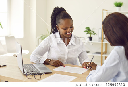 Two smiling business women working in office, reaching agreement or signing a contract. 129999810