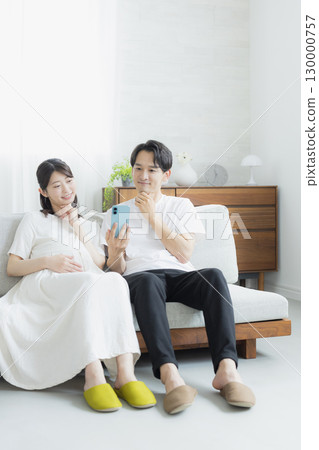 Pregnant woman in the living room, couple, smartphone 130000757