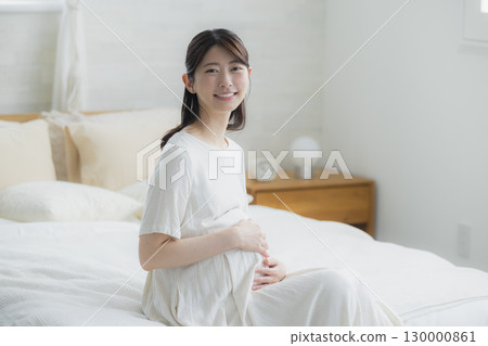 Pregnant woman sitting on bed in bedroom Pregnant woman sitting on bed in bedroom 130000861