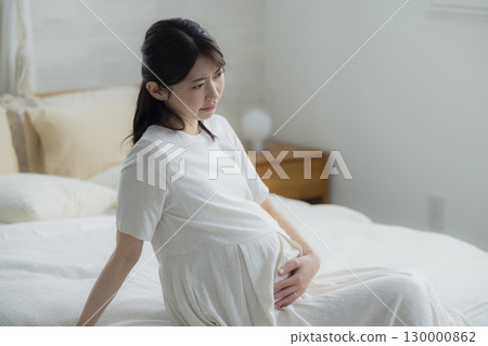 Pregnant woman sitting on bed in bedroom 130000862