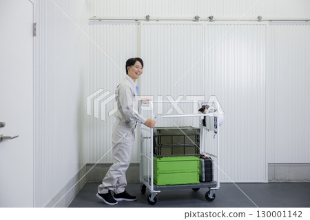 A man in work clothes pushing a cart in a warehouse A man in work clothes pushing a cart in a warehouse 130001142