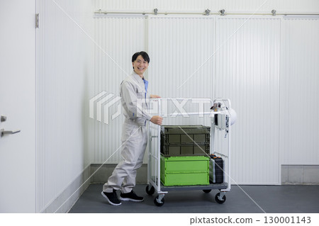 一名身穿工作服的男子在倉庫裡推著手推車 一名身穿工作服的男子在倉庫裡推著手推車 130001143