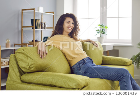 Happy young woman enjoying leisure time and relaxing on a comfortable green sofa at home 130001439