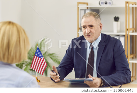 Woman sitting back in office of US public services or embassy and having visa interview. 130001443