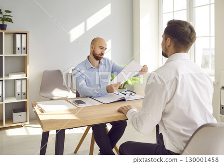 Man interviewing new candidate for vacancy company sitting in office holding and reading resume. Man interviewing new candidate for vacancy company sitting in office holding and reading resume. 130001458