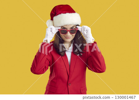 Portrait of smiling happy brunette woman is Santa hat, sunglasses and red suit on yellow background. Portrait of smiling happy brunette woman is Santa hat, sunglasses and red suit on yellow background. 130001467