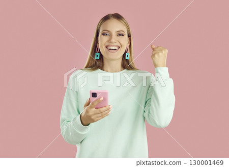 Portrait of happy girl with smartphone celebrating victory raising one fist 130001469