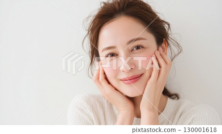 Close-up of a smiling woman holding her cheeks with both hands 130001618