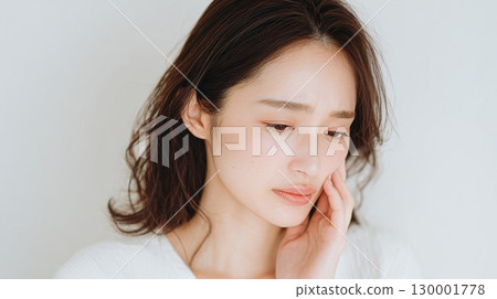 A woman holding her hand on her cheek and looking anxiously, expressing pain and worry 130001778