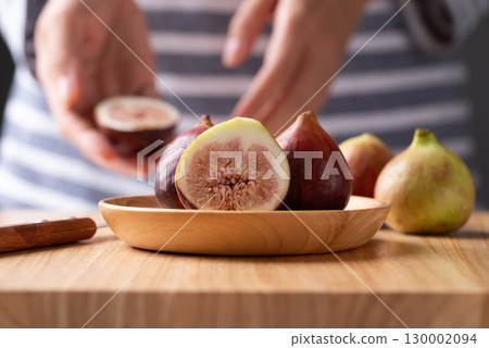 Fresh half fig and whole fruit on wooden plate and cutting wooden board with woman hand preparing 130002094