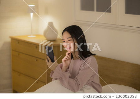 一名婦女在床上的看一個智能手機 130002358