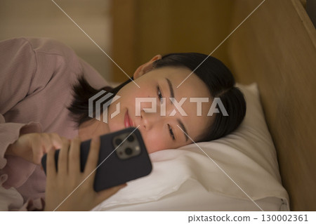 一名婦女在床上的看一個智能手機 一名婦女在床上的看一個智能手機 130002361
