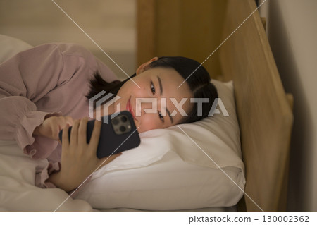 一名婦女在床上的看一個智能手機 130002362