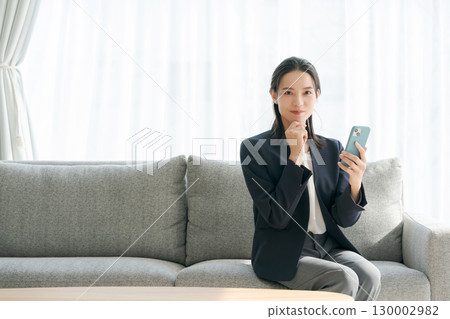 Woman sitting on sofa and using smartphone 130002982
