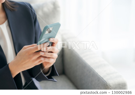 The hands of a woman sitting on a sofa and using a smartphone The hands of a woman sitting on a sofa and using a smartphone 130002986