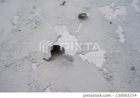 Peeling paint on gray concrete wall. Peeling, cracking, or blistering paint occurs when there is a loss of adhesion between the paint and the surface it's placed on. 130003154