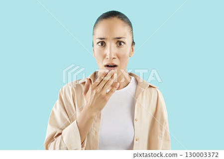Unpleasantly surprised girl on blue background covers mouth with palm, close-up 130003372