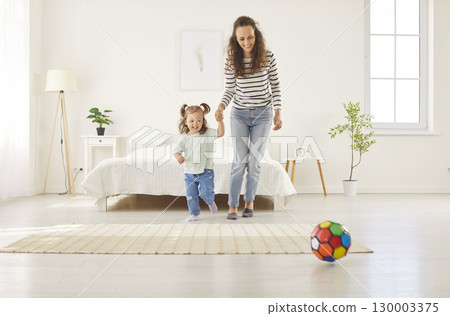 Happy mother and daughter playing with colorful ball in bedroom, holding hands and enjoying weekend. Happy mother and daughter playing with colorful ball in bedroom, holding hands and enjoying weekend. 130003375
