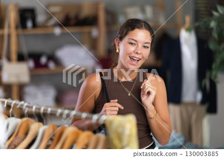 Young woman comes to boutique and looks at clothes 130003885