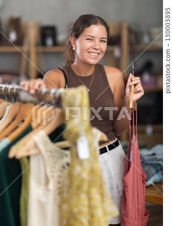 Girl customer choose dress in store, and buyer carefully examines product. 130003895