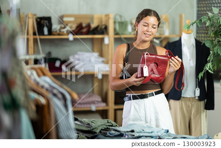Girl customer choose handbag in store, and buyer carefully examines product. Girl customer choose handbag in store, and buyer carefully examines product. 130003923