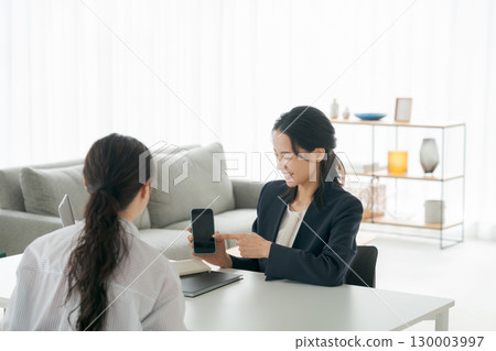 A businesswoman explaining a smartphone in the living room A businesswoman explaining a smartphone in the living room 130003997
