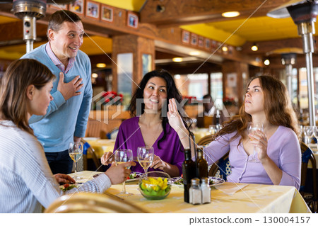 Smiling men invite women to dine for their table in restaurant 130004157