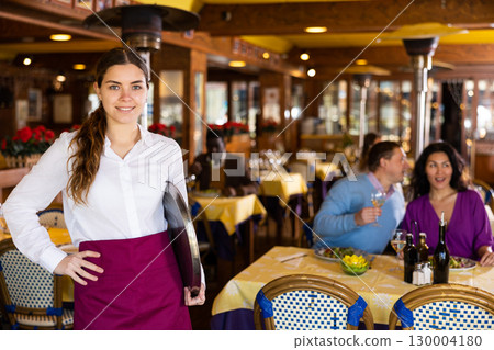 Confident smiling young waitress standing in restaurant hall Confident smiling young waitress standing in restaurant hall 130004180