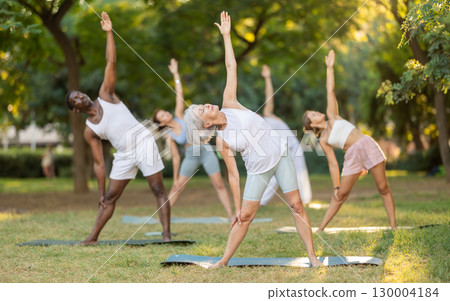 Fitness, sport and healthy lifestyle concept: group of multinational people doing yoga yoga pose - vrikshasana pose on mat in park 130004184
