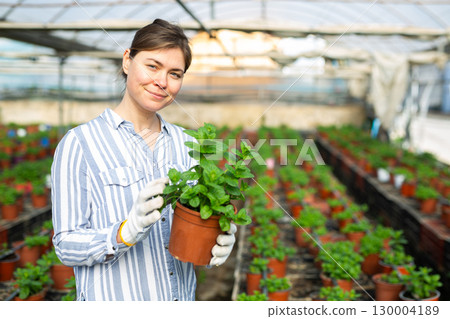 Positive gardener holding potted plant and looking at camera 130004189