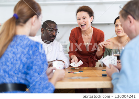 Happy woman demonstrating winning card in poker game with friends 130004241