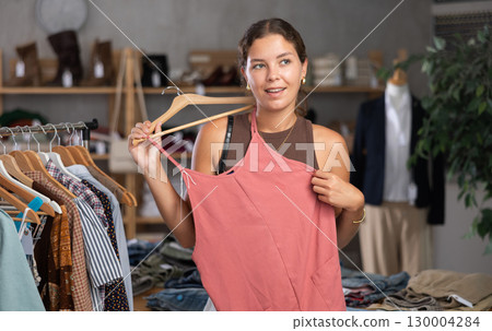 Girl customer choose crop top in store, and buyer carefully examines product. 130004284