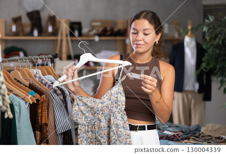 Girl customer choose crop top in store, and buyer carefully examines product. 130004339