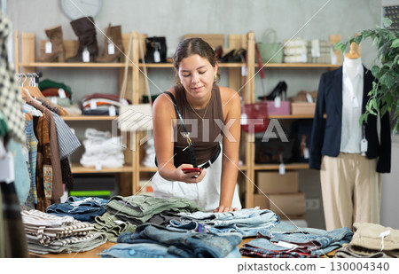 Girl scans QR code and label of denim jeans using mobile phone camera. 130004340