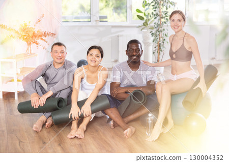 Happy portrait of group of four multinational people with mats and soft balls going to do yoga in gym 130004352