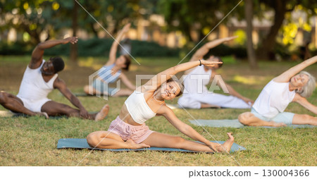 Girl stretching in Janu Sirsasana during group yoga in park Girl stretching in Janu Sirsasana during group yoga in park 130004366