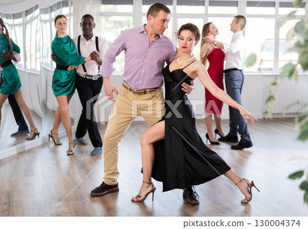 Elegant couple performs an expressive tango in bright, modern dance studio during group class 130004374