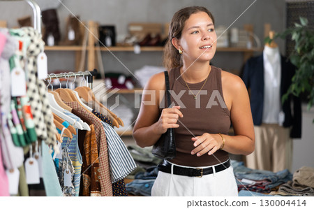 Young woman comes to boutique and looks at clothes 130004414