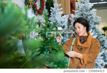 Asian woman selecting christmas tree in shop Asian woman selecting christmas tree in shop 130004423