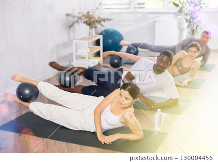 Group of active people doing soft ball pilates exercises during group pilates class in fitness gym 130004456