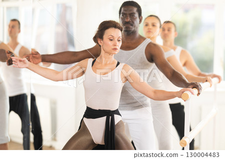 Woman performing demi plie at ballet barre at group training 130004483