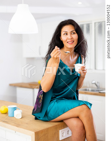 Portrait of positive woman in nightdress eating yogurt at home Portrait of positive woman in nightdress eating yogurt at home 130004552