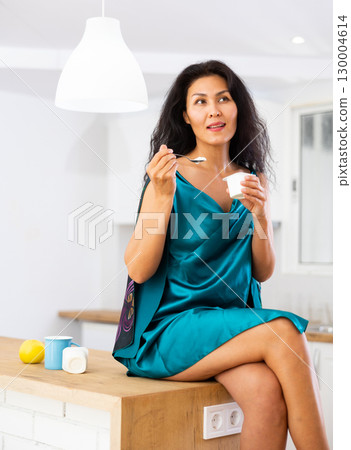 Portrait of positive woman in nightdress eating yogurt at home Portrait of positive woman in nightdress eating yogurt at home 130004614
